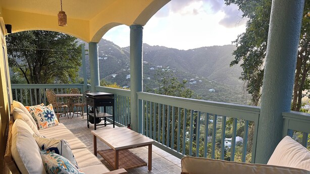 Un balcone con divano, sedie e tavolo, con vista su un paesaggio montuoso.