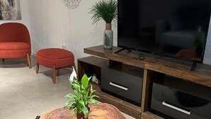 A modern living room with a wooden coffee table, a red chair, a TV on a wooden stand, and a potted plant. - Oceanfront Beach House at Parada 23 La Mansa - Direct Beach Access (Punta del Este)