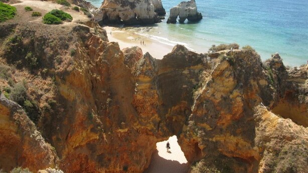 Eine Küstenlandschaft mit schroffen Klippen, einem Strand und klarem, blauem Wasser.