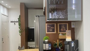 A modern kitchen with a coffee machine, a refrigerator, and a glass display cabinet. - Apartment - Jewel Ingleses Santinho 5 minutes from the beach (Florianópolis)