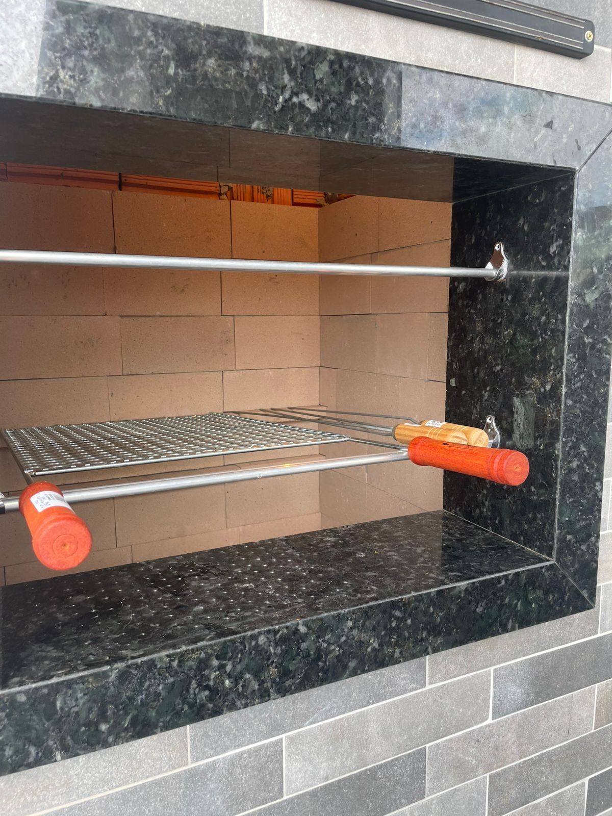 A brick oven with a metal rack and a long-handled tool.
