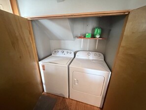 A laundry room with two white washing machines and a shelf with a green bottle.