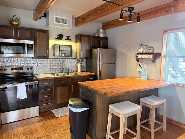 A modern kitchen with wooden cabinets, stainless steel appliances, and a wooden island with stools.