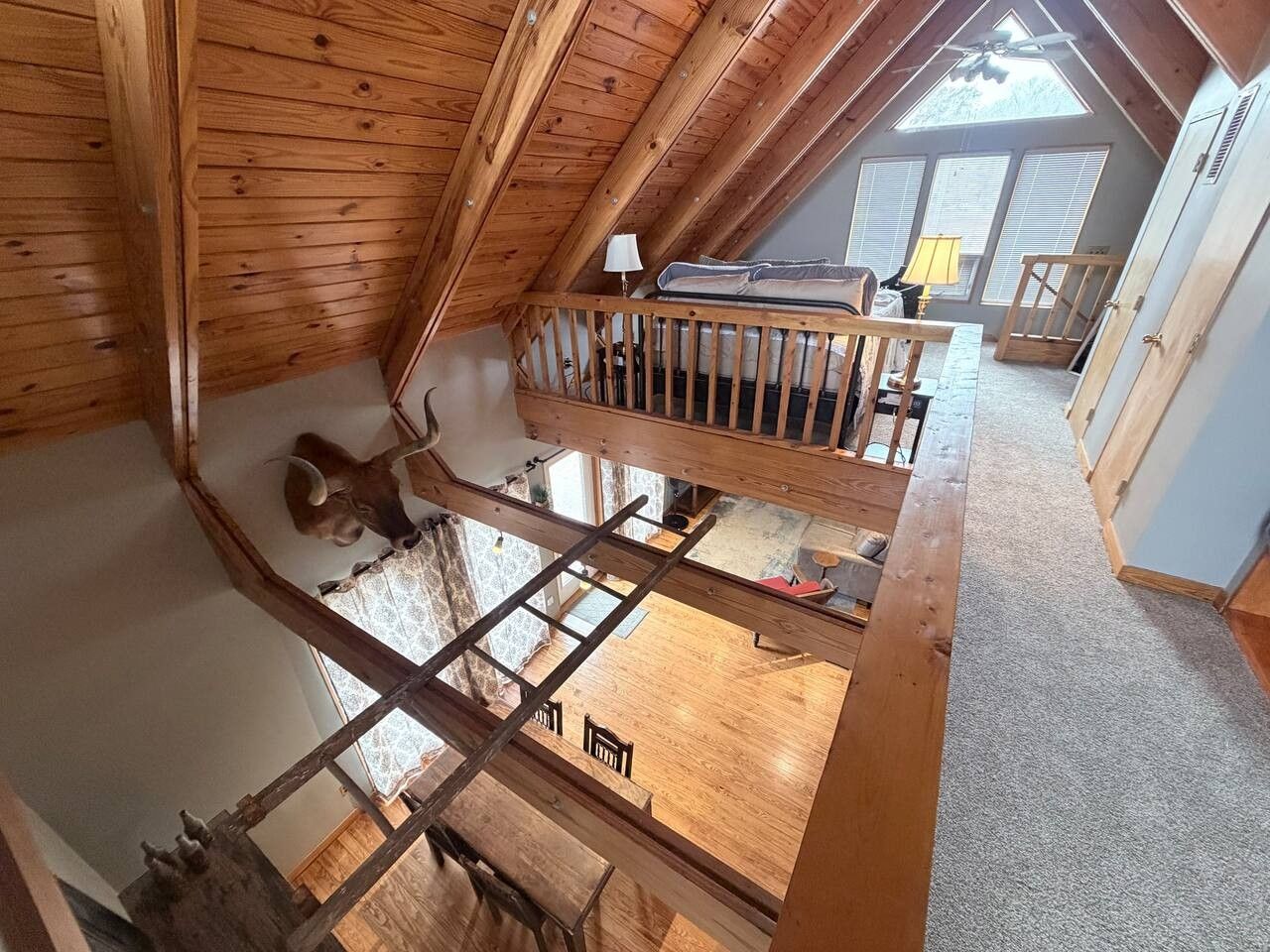 A loft bedroom with a sloped ceiling, wooden beams, a bunk bed, a ladder, and a view of the adjacent room.
