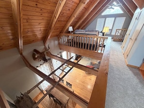 A loft bedroom with a sloped ceiling, wooden beams, a bunk bed, a ladder, and a view of the adjacent room.