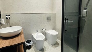 Ein modernes Badezimmer mit einem hölzernen Waschtisch, einem weißen Waschbecken, einem Bidet, einer Toilette und einer Dusche mit Glaswand.
