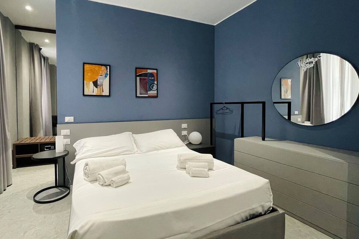 A modern hotel room with a large bed, a round mirror, and two framed artworks on the wall.