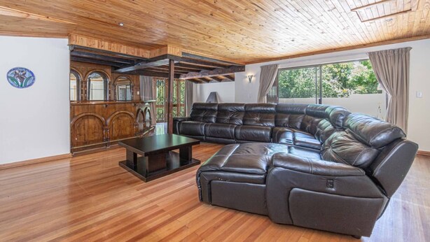 A spacious living room with a large L-shaped leather sofa, wooden flooring, and a wooden ceiling. - Super Spacious Fun Home! With Pool, Den and Bar (Johannesburg)