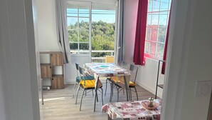 A room with a dining table, chairs, a sofa, and a window with curtains.