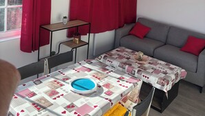 A room with a dining table, a sofa, and a window with red curtains.