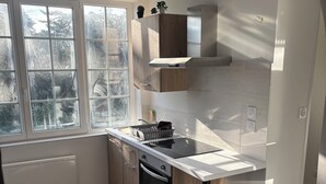 A modern kitchen with a large window, wooden cabinets, a built-in oven, and a stainless steel countertop.