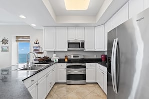 A modern kitchen with white cabinets, stainless steel appliances, and a large window with a view. - San Carlos 1509| Beach Front (Gulf Shores)