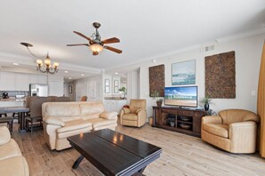 A spacious living room with a ceiling fan, a dark wooden coffee table, beige sofas, and a television. - San Carlos 1709| Beach Front (Gulf Shores)
