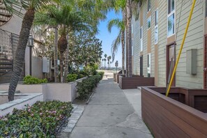A narrow pathway flanked by wooden planters and palm trees, leading to a building with a beige facade and windows. - 1 Block to Bay - Boutique 1BR with Parking - Mission Beach (San Diego)