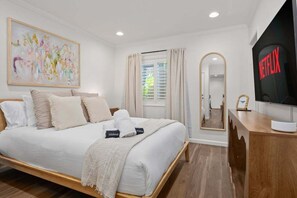 Quarto de hotel moderno com uma cama, televisão, espelho e janela com cortinas.