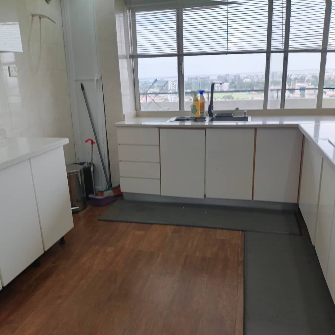 Eine Küche mit weißen Schränken, einem Fenster mit Jalousien, einem Mop und Reinigungsmitteln.