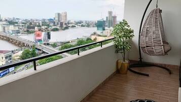 Un balcón con vista a un paisaje urbano, una silla colgante, una planta en maceta y un felpudo estampado.