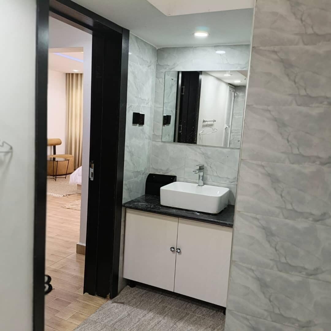 Ein modernes Badezimmer mit einem weißen Waschbecken, dunklen Schränken und einer Marmor-Spritzschutzwand.