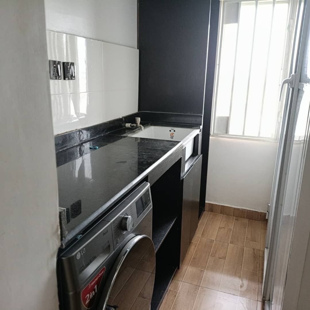 A compact kitchen with a black countertop, a built-in oven, and a window with blinds.
