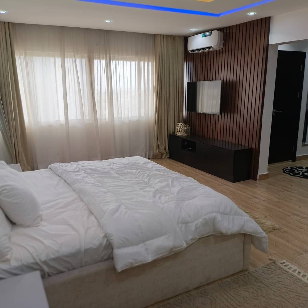 Ein Schlafzimmer mit Bett, Vorhängen, einer Klimaanlage, einem Schminktisch und einer Tür.