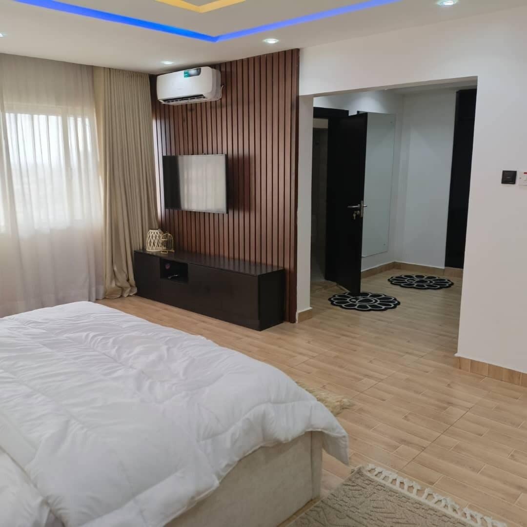 A bedroom with a bed, a dresser, an air conditioning unit, and a door leading to another room.