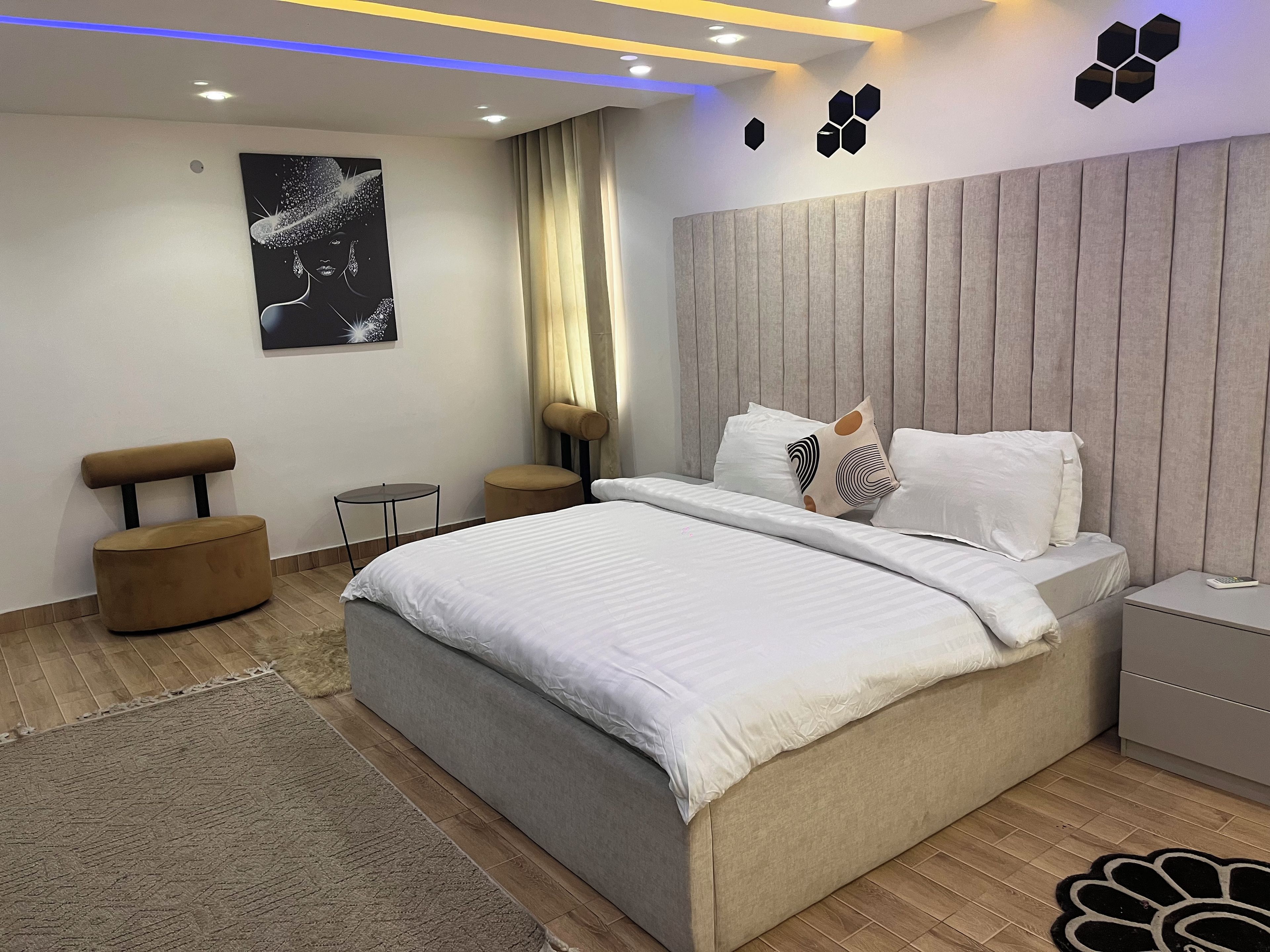 Une chambre moderne avec un grand lit, une tête de lit, une petite table, une chaise et un élément décoratif mural.