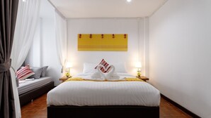 Ein ordentlich eingerichtetes Hotelzimmer mit einem großen Bett, zwei Nachttischlampen, einem gelben Wandbild und einem kleinen Nachttisch mit Blumen.