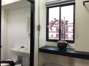 A bathroom with a white sink, a toilet, and a window with an orchid plant. - Huenphen House And Cafe' (Chiang Mai)
