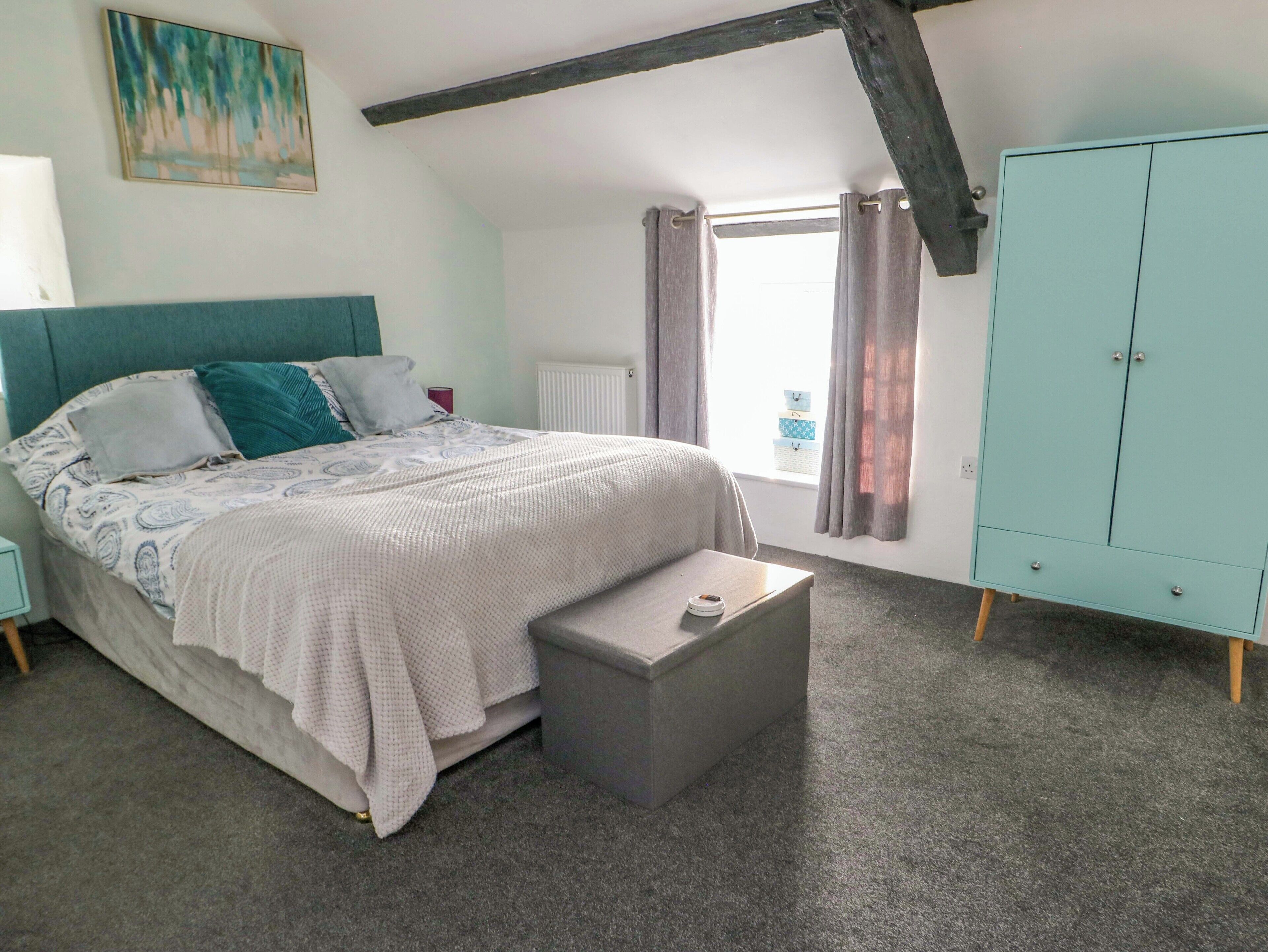 A bedroom with a bed, a nightstand, a dresser, and a window with curtains.