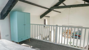 A bedroom with a white bed, a teal wardrobe, a white railing, and a view of a colorful mural. - The Mill (Holyhead)