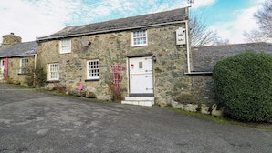 A stone building with a white door, windows, and a small porch area. - The Mill (Holyhead)