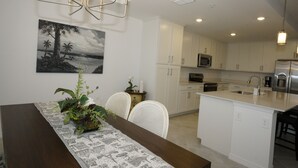 Uma cozinha moderna com armários brancos, uma ilha central com pia e uma área de jantar com mesa e cadeiras de madeira.