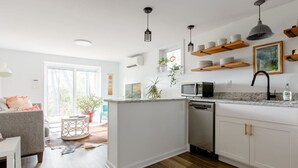 A modern kitchen with white cabinetry, a built-in microwave, and a dishwasher. There are wooden shelves above the counter holding dishes.