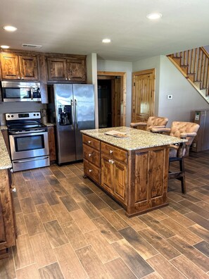 A kitchen with wooden cabinets, stainless steel appliances, and a herringbone-patterned floor. - Ozark Getaway at The White River! (Flippin)