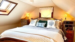 A bedroom with a large bed, wooden headboard, two bedside tables with lamps, a window with curtains, and a skylight. - Heaven on Cranberry in Dennisport: Perfect for Families-1/2 mile to Beach (Dennis)
