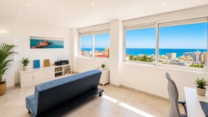 Una habitación moderna con sofá, mesa de comedor y vistas al mar y al paisaje urbano.