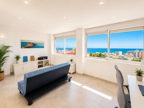 Ein modernes Zimmer mit Sofa, Esstisch und Blick auf das Meer und die Stadtlandschaft.