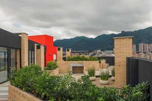 A rooftop garden with a modern design, featuring a red structure, brick walls, and various plants. - C60 Rentals (Bogotá)