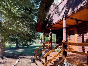 Eine Holzhütte mit Veranda, Holzstufen und Blick auf eine bewaldete Landschaft.