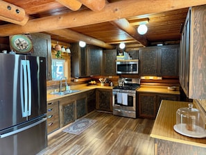 Ein Holzblockhaus-Interieur mit einem Edelstahl-Kühlschrank, einer Mikrowelle, einem Backofen und einem Waschbecken.