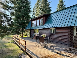 Eine Blockhütte mit einer Holzdachterrasse, Sitzgelegenheiten im Freien und einem Metalldach.