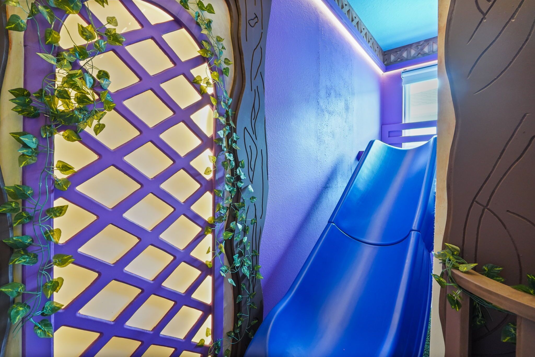 A room with a purple lattice door, a blue slide, and a wall with a geometric pattern.