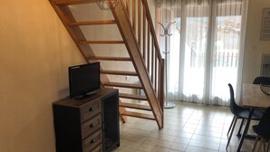 Una stanza con una scala in legno, una televisione su un mobile, un tavolo da pranzo con sedie e una finestra con tende.