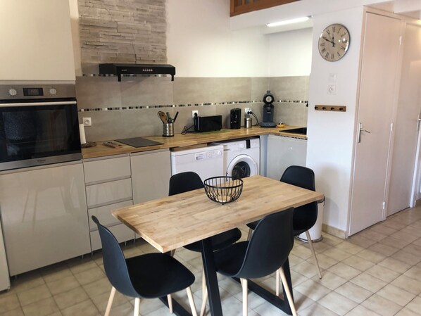 A compact kitchen with a microwave, oven, dishwasher, and a wooden table with chairs.