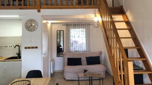 Un appartamento in stile loft con una scala in legno, una zona giorno con un divano e un tavolino, e un angolo cottura con un lavello e una sveglia.