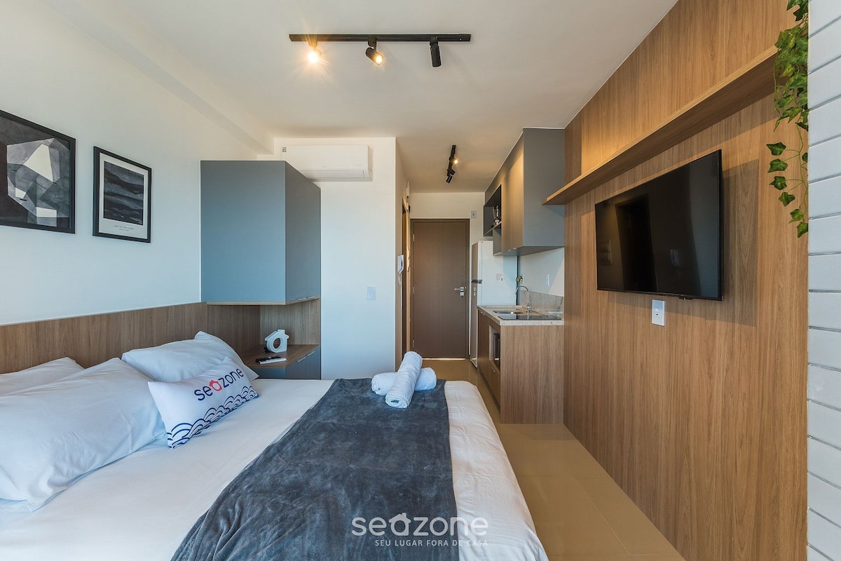 A modern hotel room with a bed, a TV, a sink, and a shower area.