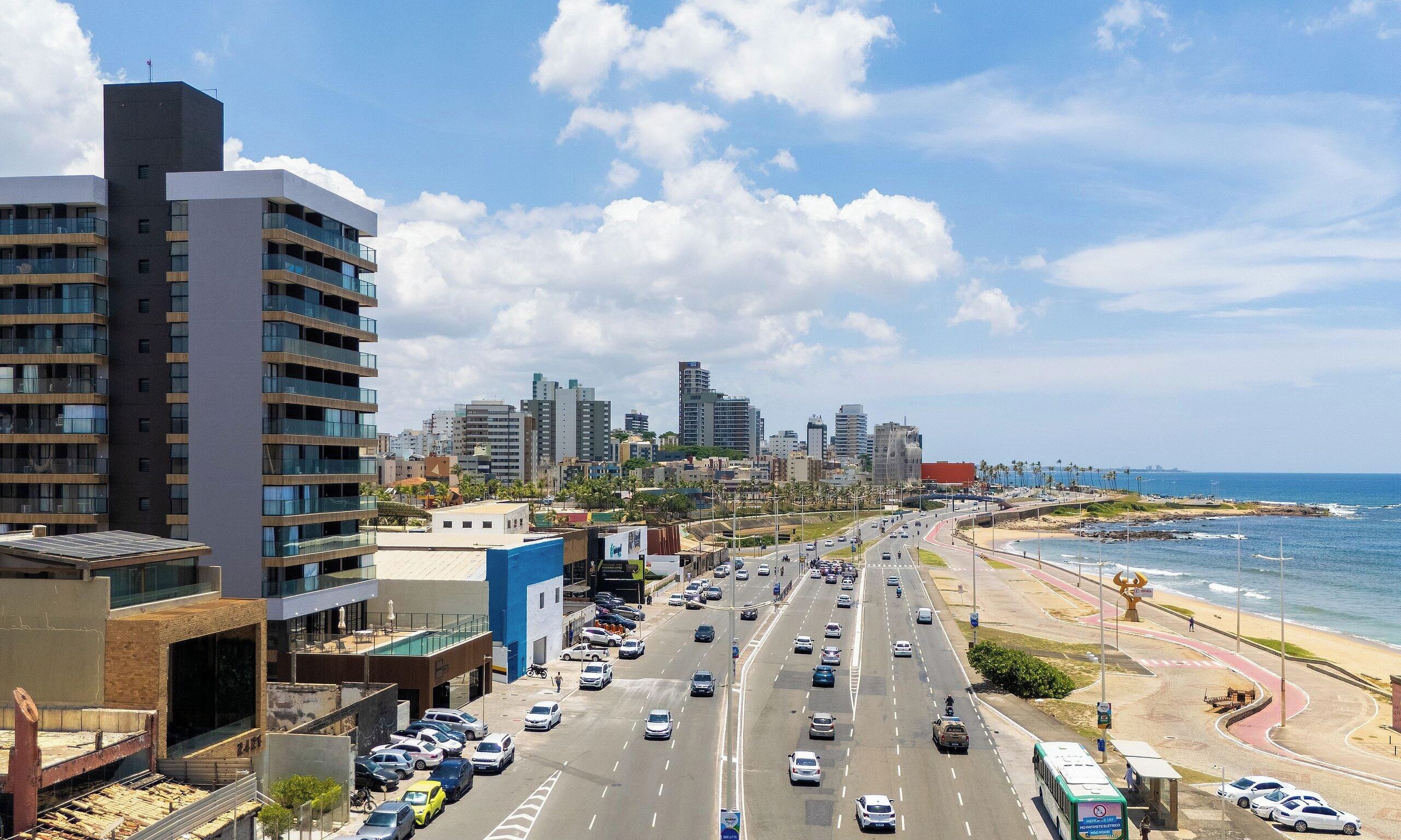 A coastal cityscape with modern buildings, a busy road, and a beach.
