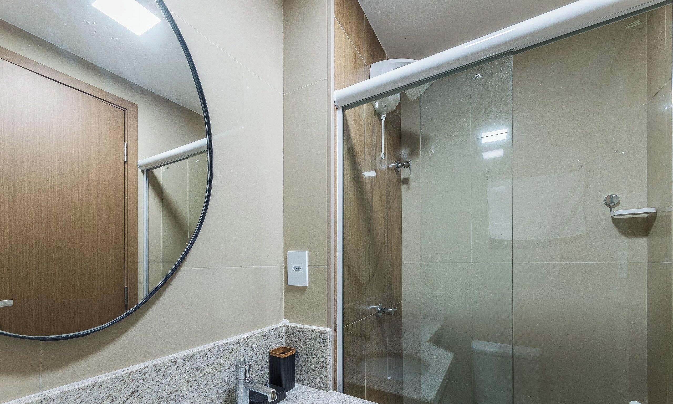 Une salle de bain avec une douche à parois de verre, un miroir rond et un meuble en bois.