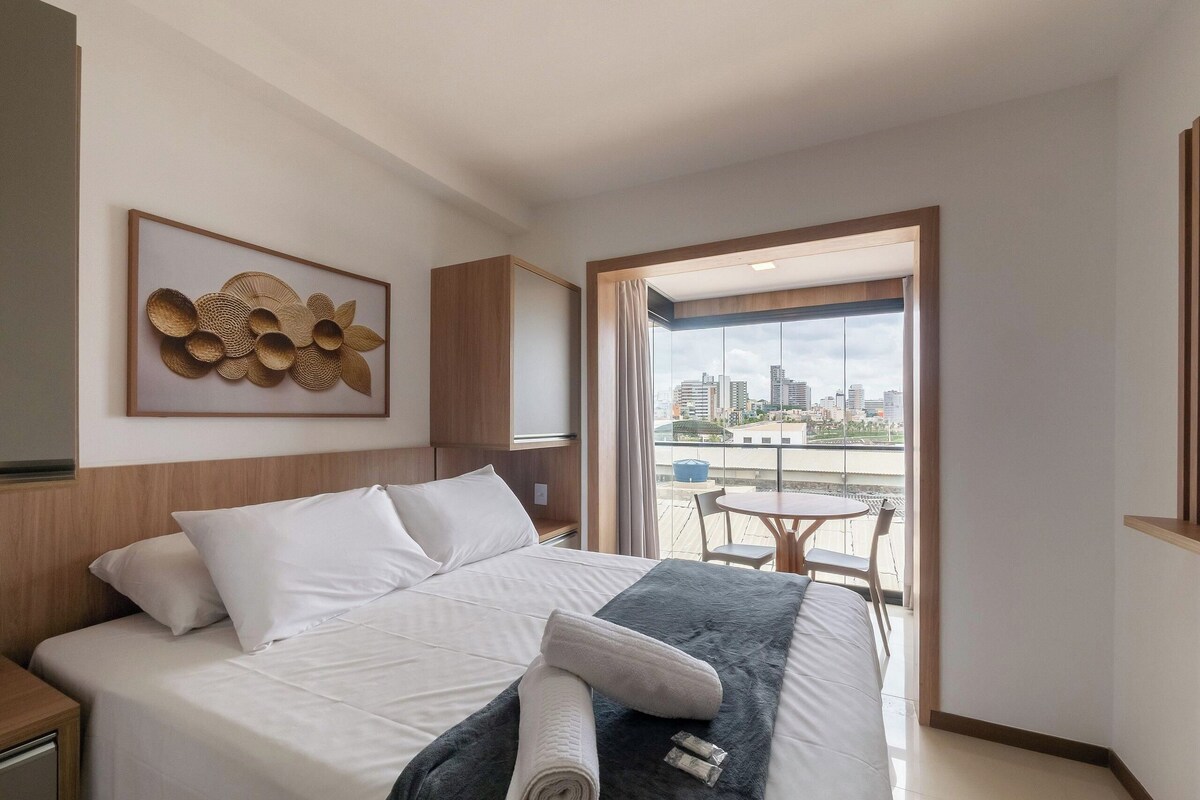 A hotel room with a bed, a view of the city, and a balcony with a table and chairs.