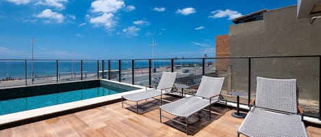 Un área de piscina en la azotea con sillones de descanso y vistas a la playa.